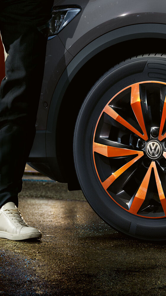 Um homem caminha para o seu carro VW cinzento com jantes VW polidas com acentos de cor laranja 