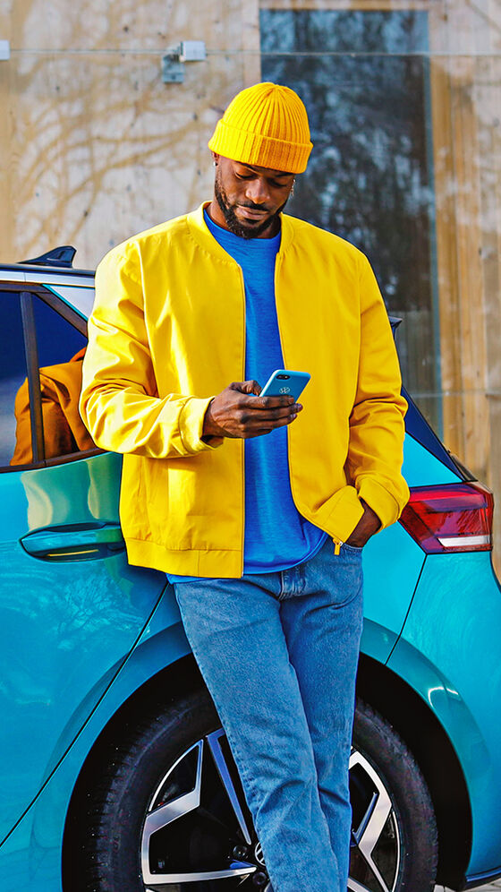 Ein Mann in einer gelben Jacke lehnt an seinem VW ID