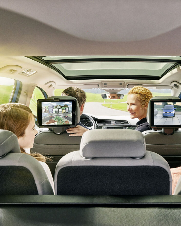 Innenansicht eines VW - auf den Kopfstützen von Fahrer und Beifahrer sind Tablets mithilfe des VW Tablet-Halters montiert. Vorne sitzen die Eltern, hinten die Kinder.
