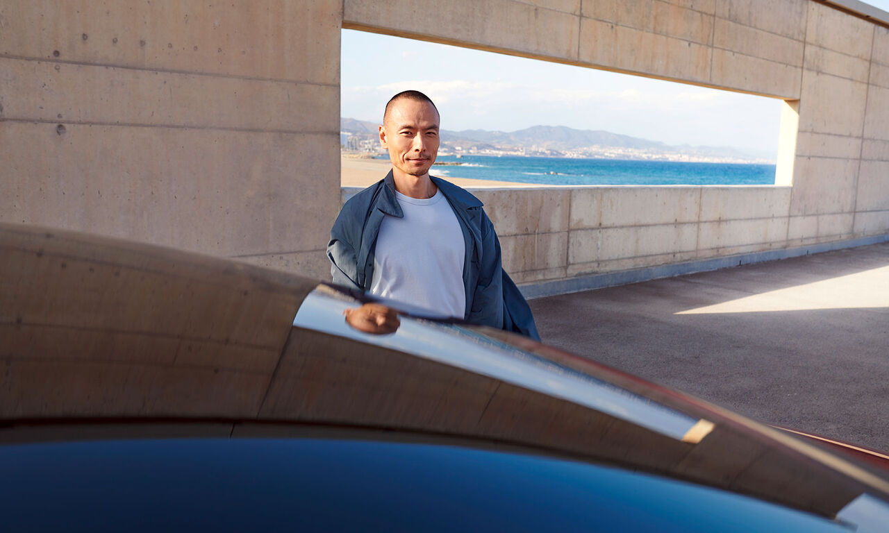 Homem em frente de uma parede de betão, janela em segundo plano mostra uma paisagem costeira. Em primeiro plano, tejadilho do VW ID.5 GTX.