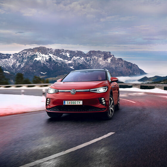 VW ID.4 GTX em vermelho visto de frente. Em andamento numa estrada de campo nas montanhas cobertas de neve.