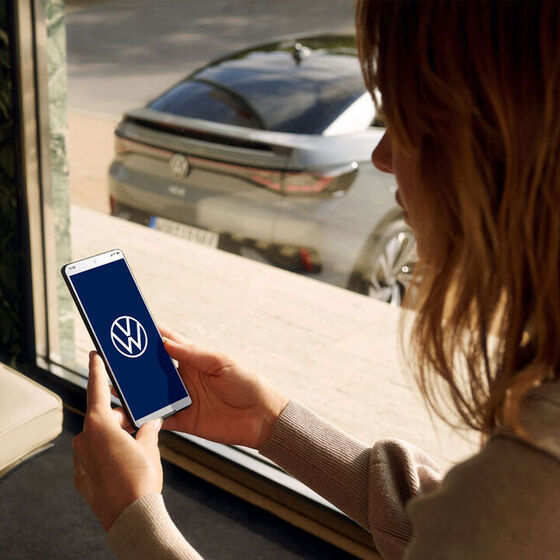Eine Frau schaut auf ihr Smartphone mit VW Logo – Over-the-Air Update
