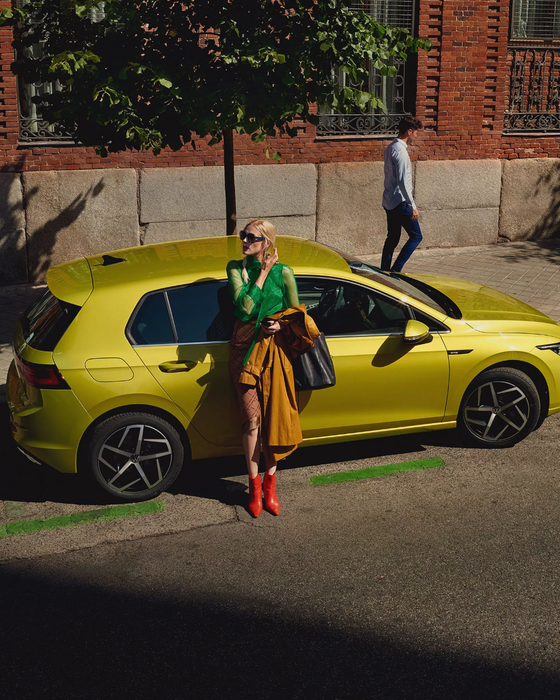 VW Golf estacionado na berma da estrada, uma mulher encostada à porta lateral