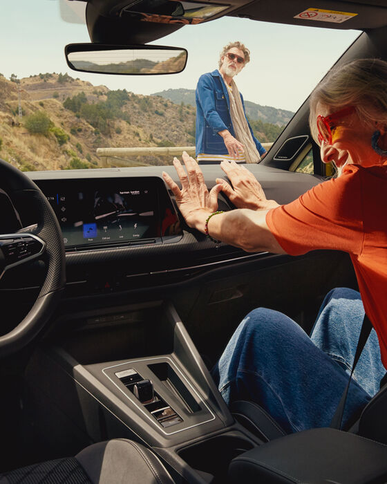 Vista interior do VW Golf com uma mulher sentada no lugar do pendura; está um homem de fora a observar
