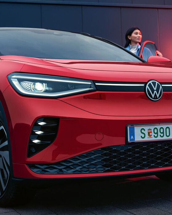 VW ID.4 GTX em vermelho durante o carregamento. Mulher de pé ao seu lado.