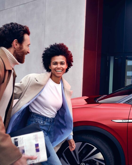 VW ID.4 GTX em vermelho na berma da estrada. Homem e mulher caminham sorridentes.