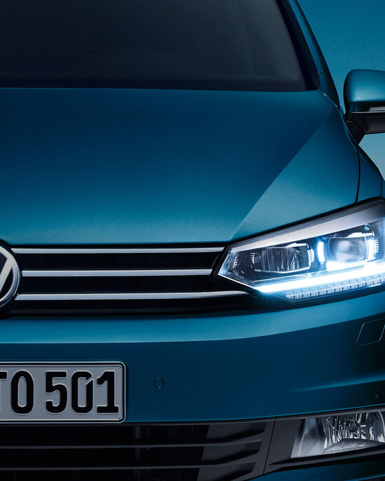 Frente do VW Touran ao anoitecer com faróis LED; luzes de circulação diurna ligadas.