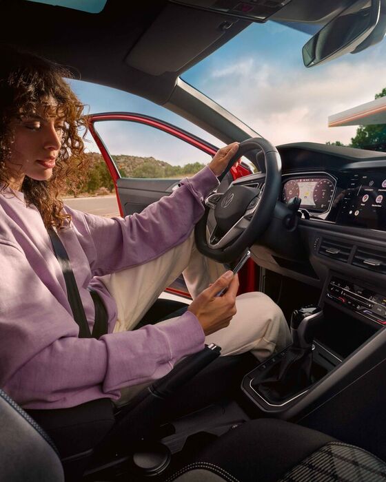 Interior do VW Taigo: Mulher sentada no lugar do condutor, no carro estacionado, a olhar para o smartphone