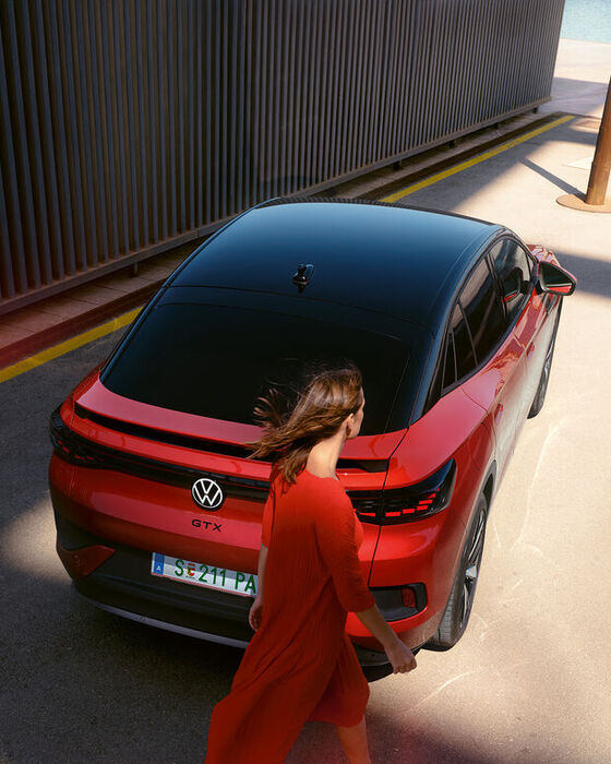 VW ID.5 GTX vermelho numa estrada secundária. Vista de cima sobre o tejadilho e a traseira. Uma mulher jovem vai a passar.