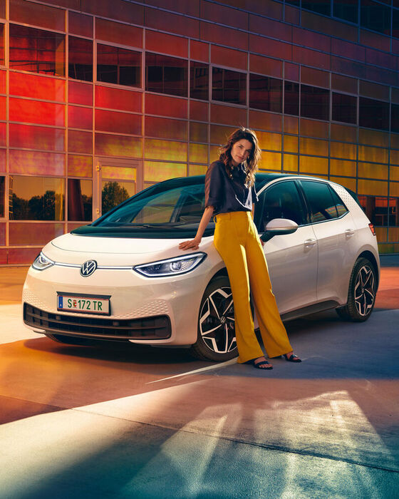 VW ID.3 em branco, vista frontal com faróis e jantes opcionais Andoya, uma mulher está encostada ao carro.
