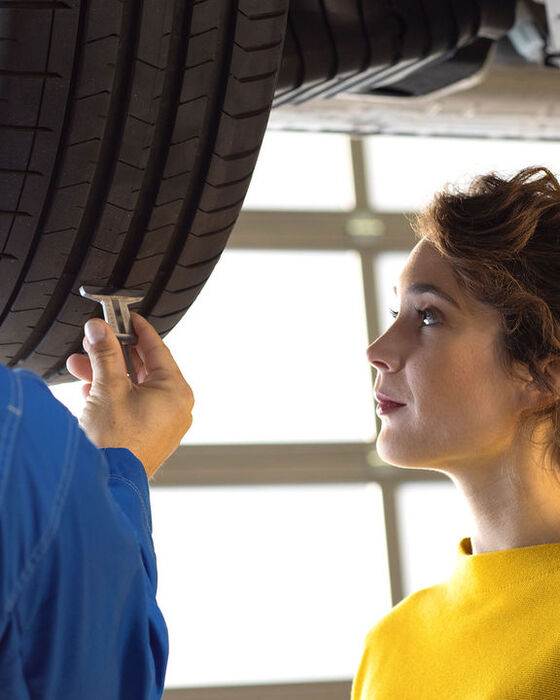 Uma mulher e um funcionário de serviço VW a medir a profundidade do piso do pneu do seu VW