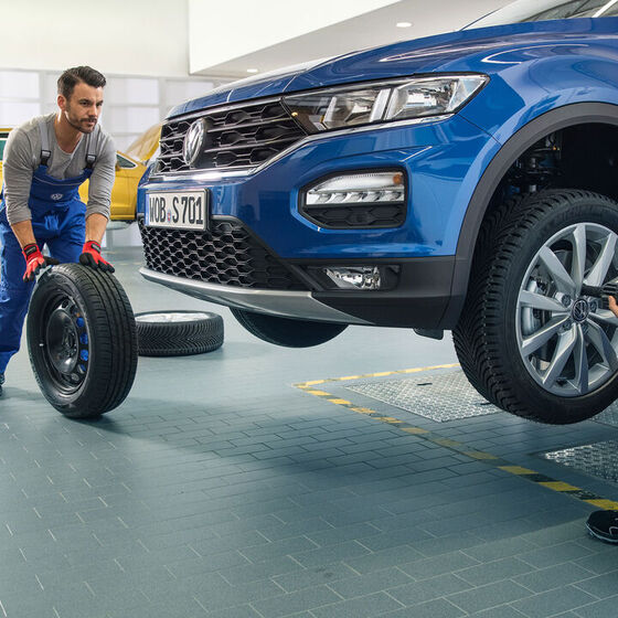 Dois empregados do serviço VW trabalham juntos na troca de pneus de um VW Tiguan azul numa oficina