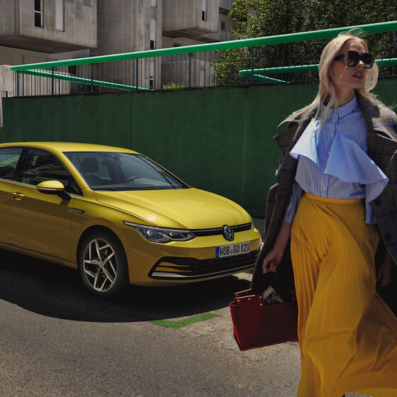 Vista traseira do VW Golf amarelo com um casal. A mulher sai do lugar do condutor.