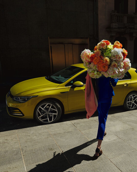 Mulher em frente a um VW Golf amarelo com os faróis LED ligados; IQ.LIGHT.