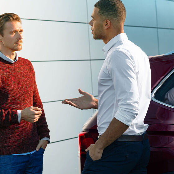 Um homem fala com um funcionário do serviço VW ao lado do seu VW vermelho