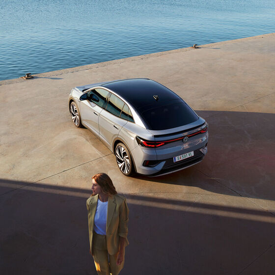 Vista superior oblíqua da traseira de um VW ID.5 no cais de um porto, em primeiro plano vê-se uma mulher