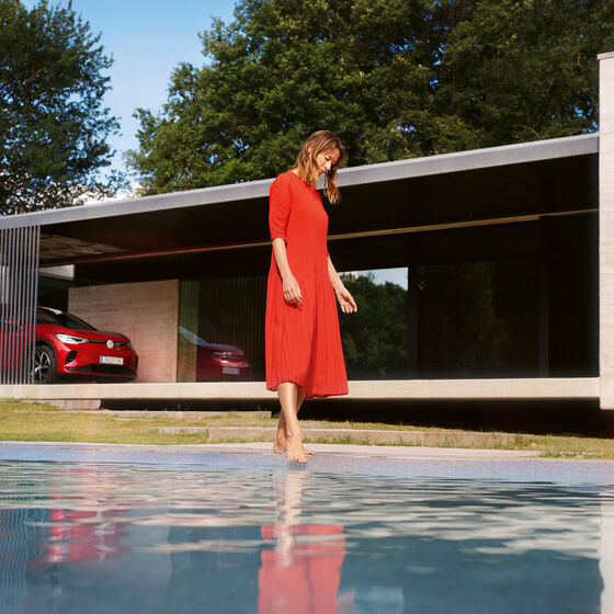 VW ID.5 GTX vermelho a estacionar em frente de uma casa. Mulher de vestido vermelho junto à piscina.