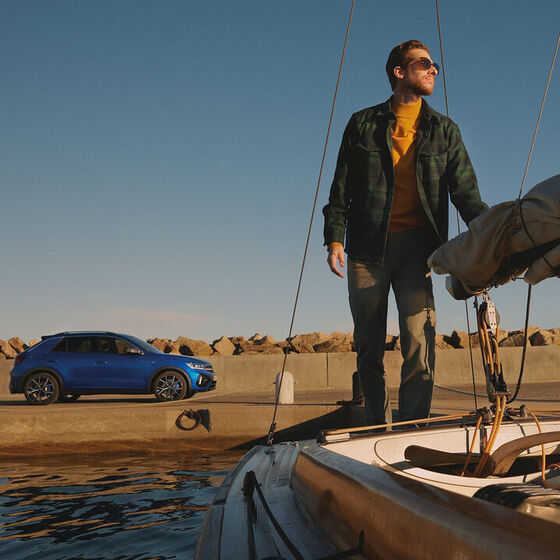 Um homem está de pé num barco e o VW T-Roc R está estacionado em segundo plano