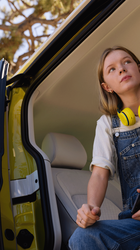 Um rapariga com auriculares amarelos sentada na porta lateral do VW ID. Buzz.