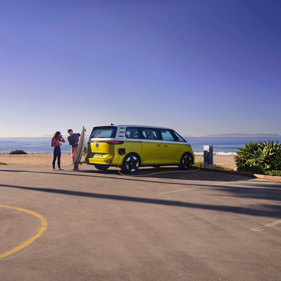 O VW ID. Buzz estacionado na praia, um homem mostra uma prancha de surf à filha.