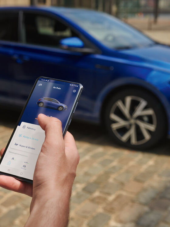 Vista do ecrã de um telemóvel com dados de veículo do Polo; em segundo plano, o VW Polo azul, estacionado.