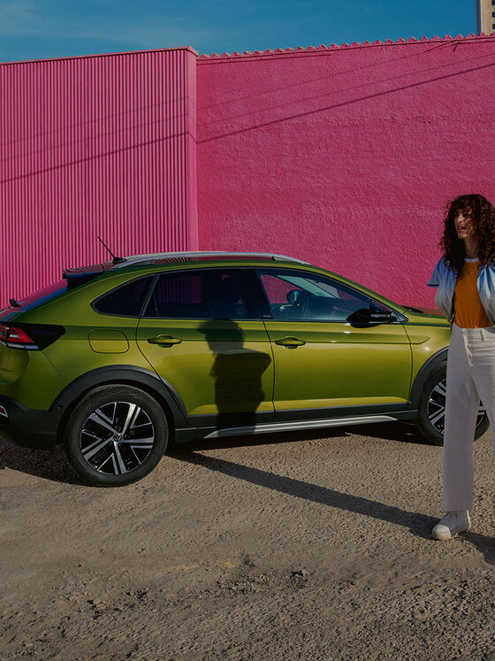 Vista lateral de VW Taigo verde num parque de estacionamento; mulher em pé em frente do automóvel