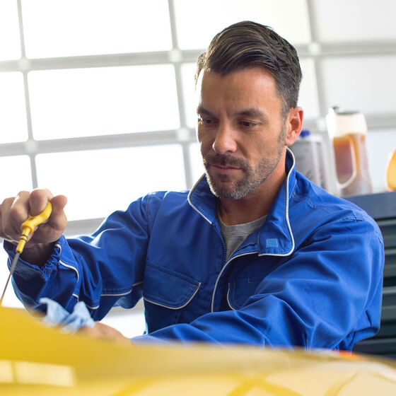 Um empregado da Volkswagen mede o nível de óleo de um carro amarelo VW numa oficina.