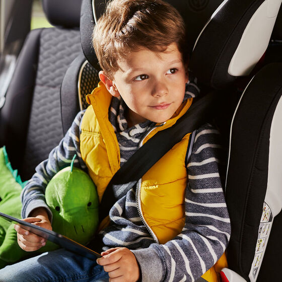Uma criança feliz com um dinossauro de peluche senta-se numa cadeira de criança VW num carro